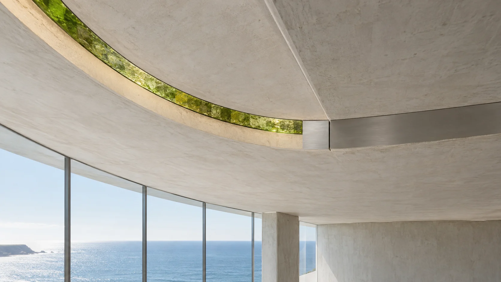 The underside of a curved concrete canopy with one long curved roof light of green-gold glass let into it, above a glazed wall and the sea.