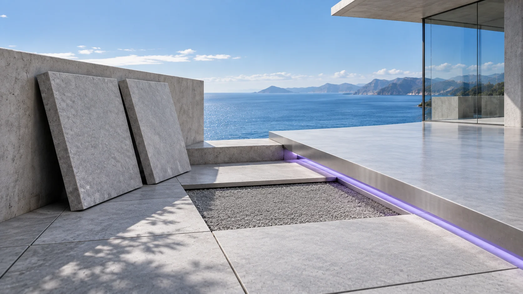 Two stone slabs leaning against a terrace wall beside an empty bed of gravel in the paving, with a line of violet light under the edge of the next terrace and the sea beyond.