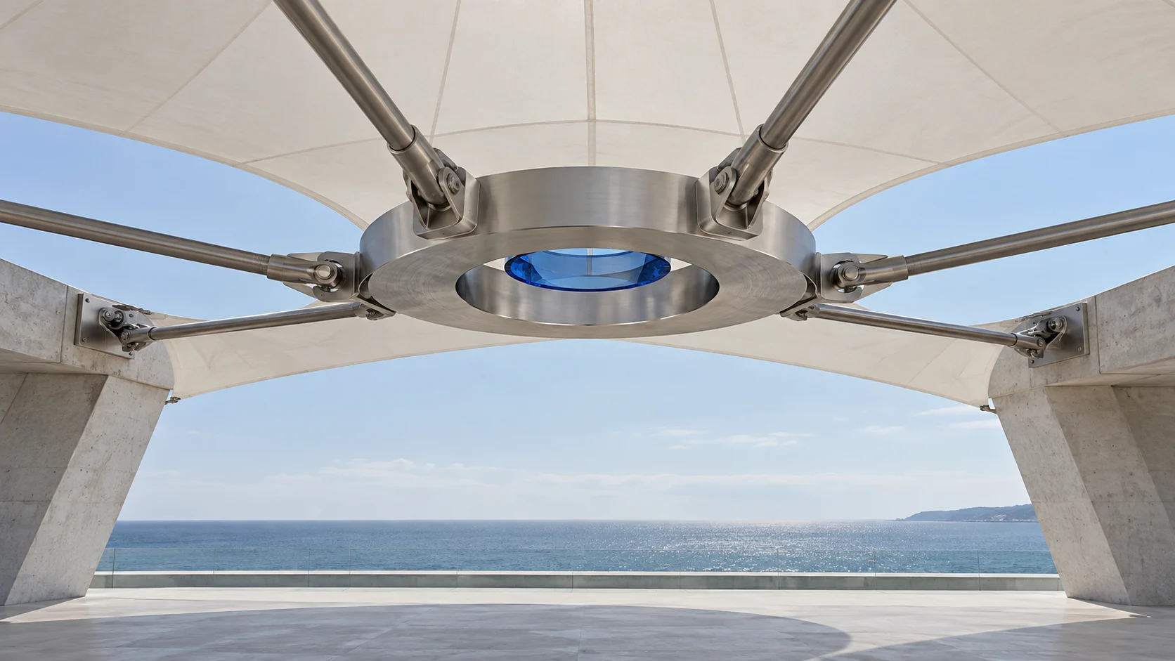 Close on the hub under the canopy: a machined steel ring with steel rods meeting it from every side, and a disc of sapphire glass at the centre. The sea lies beyond.
