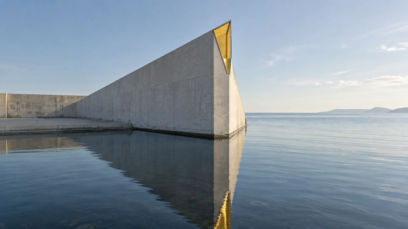 A concrete wall rising to a sharp point above still water, a tip of citrine glass at its top, its long reflection lying on the water towards the open sea.