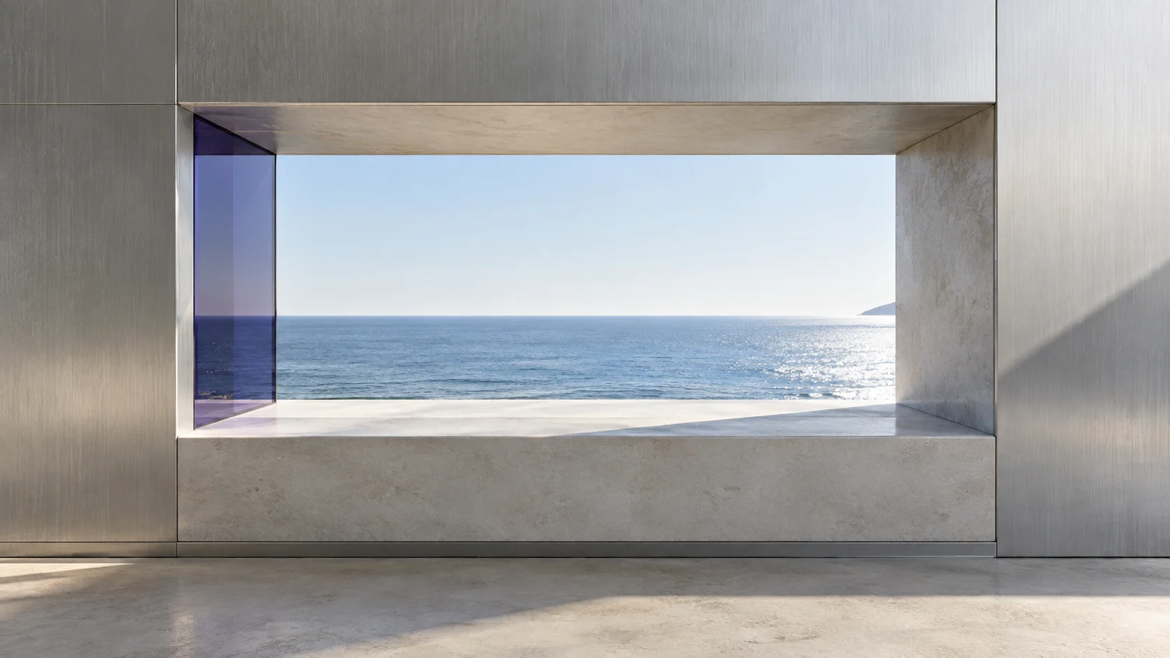 A wide opening cut through a wall faced in brushed steel, framing the sea, with a pane of iolite glass at its left edge and a stone sill below.