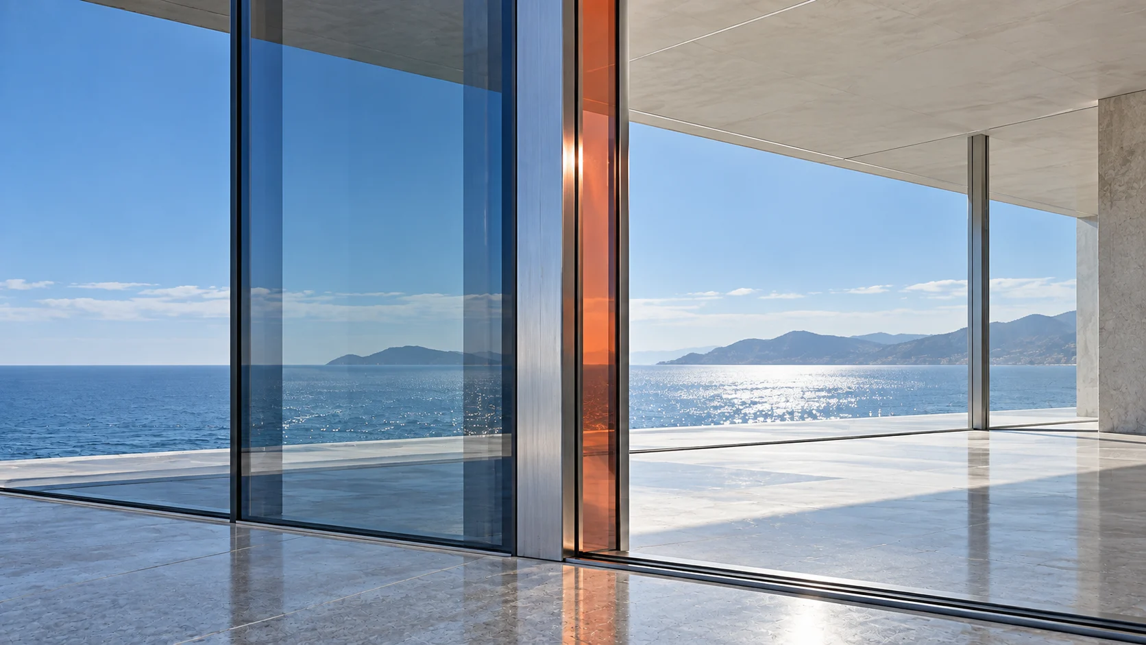 A glass facade in daylight where two bays meet at a brushed-steel mullion: one bay is tinted, the next is clear and open to the terrace, and a fin of carnelian glass stands at the mullion.