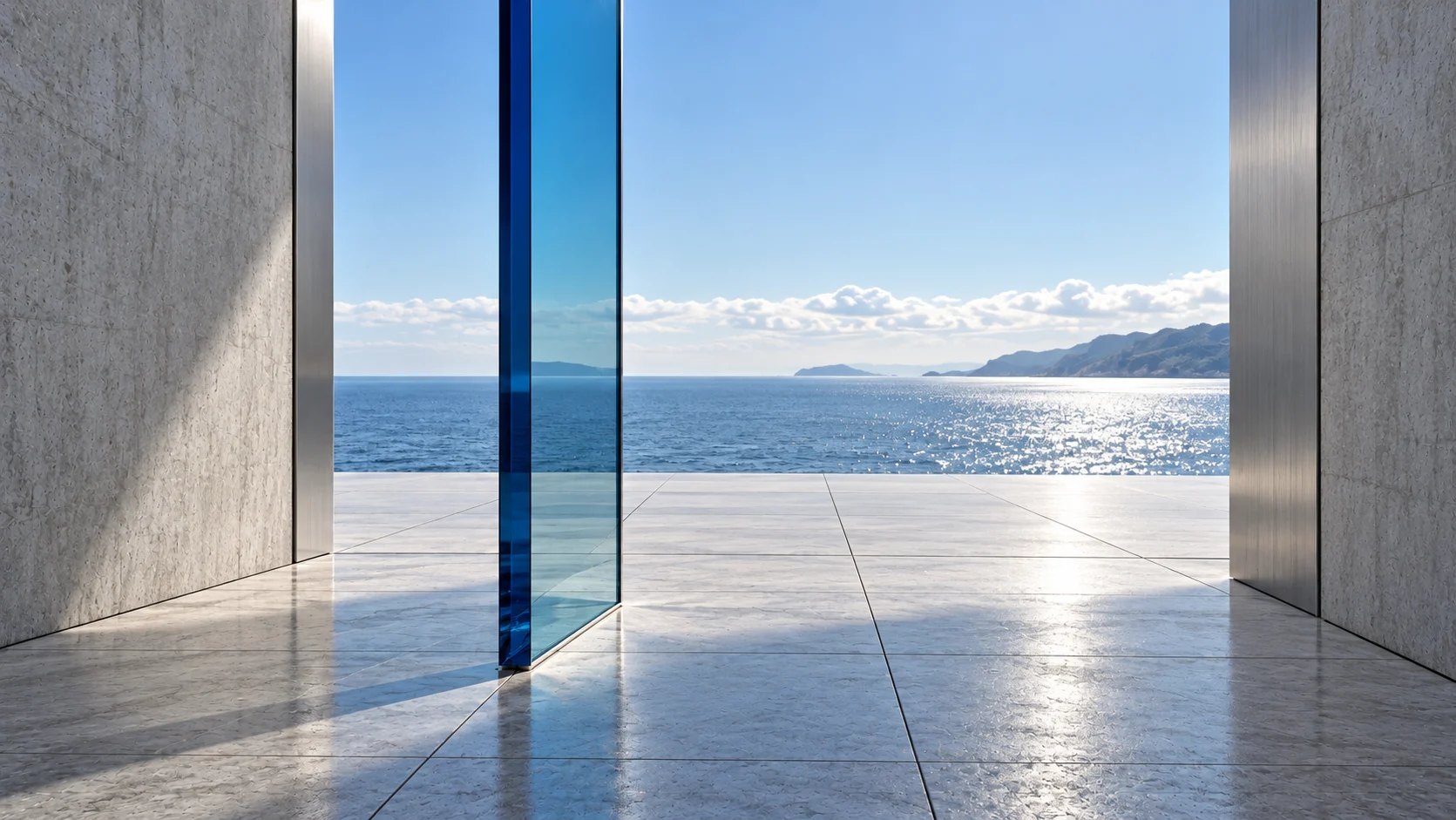 From inside the passage, beside the tall sapphire glass pane, looking out of its wide mouth onto a stone terrace of large square pavers, with the sea and a headland beyond.